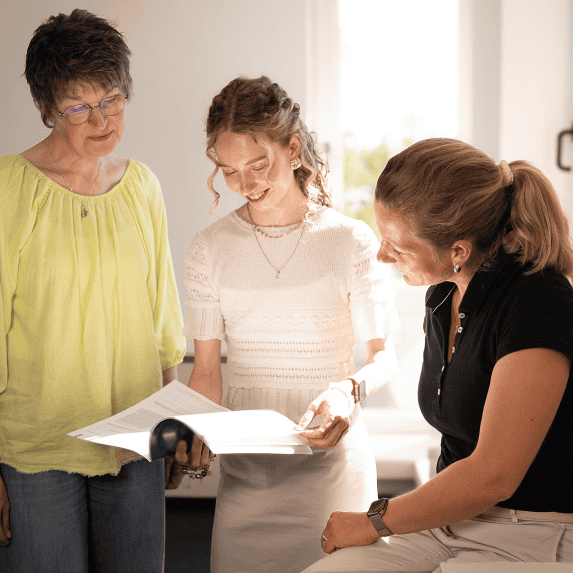 Drei Mitarbeiterinnen besprechen gemeinsam Unterlagen in heller Büroatmosphäre.