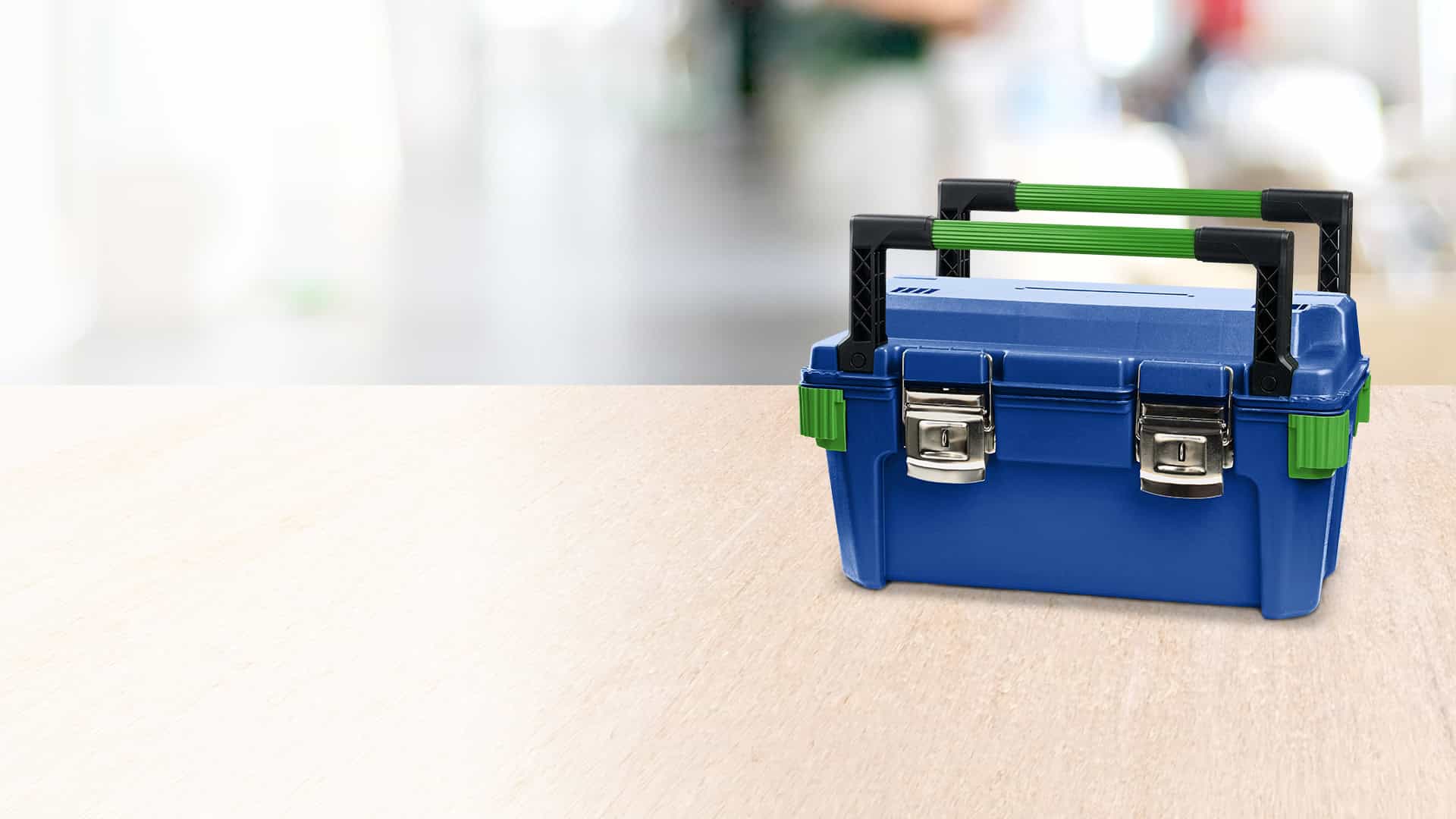 Blauer Werkzeugkoffer mit grünen Griffen und Metallverschlüssen auf einer hellen Arbeitsfläche.