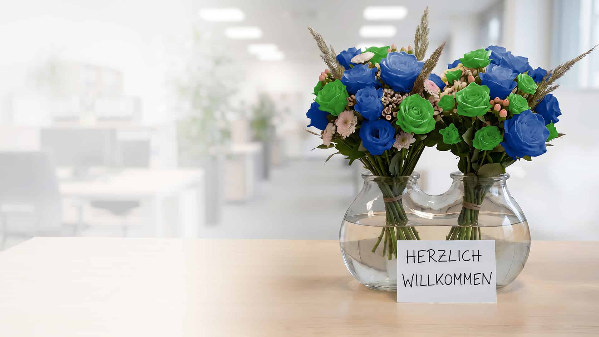 Zwei Blumensträuße mit blauen und grünen Rosen in einer Glasvase, davor eine Karte mit der Aufschrift „Herzlich willkommen“.